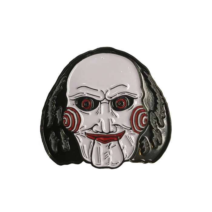 This is a Saw Billy enamel pin from Trick Or Treat and he has a white face, black hair, red lips and eyes and bullseye cheeks.