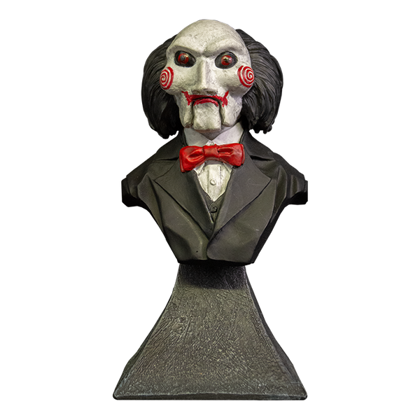 This is a Saw Billy mini bust and he has a white face, red eyes and lips, red cheek bullseyes, red bowtie, black suit and he is on a grey stand.