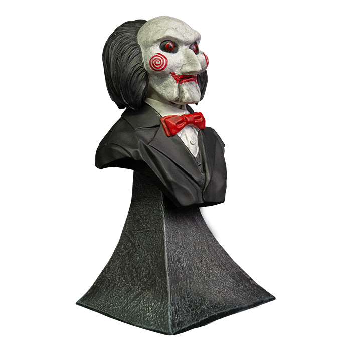 This is a Saw Billy mini bust and he has a white face, red eyes and lips, red cheek bullseyes, red bowtie, black suit , black hair and he is on a grey stand.