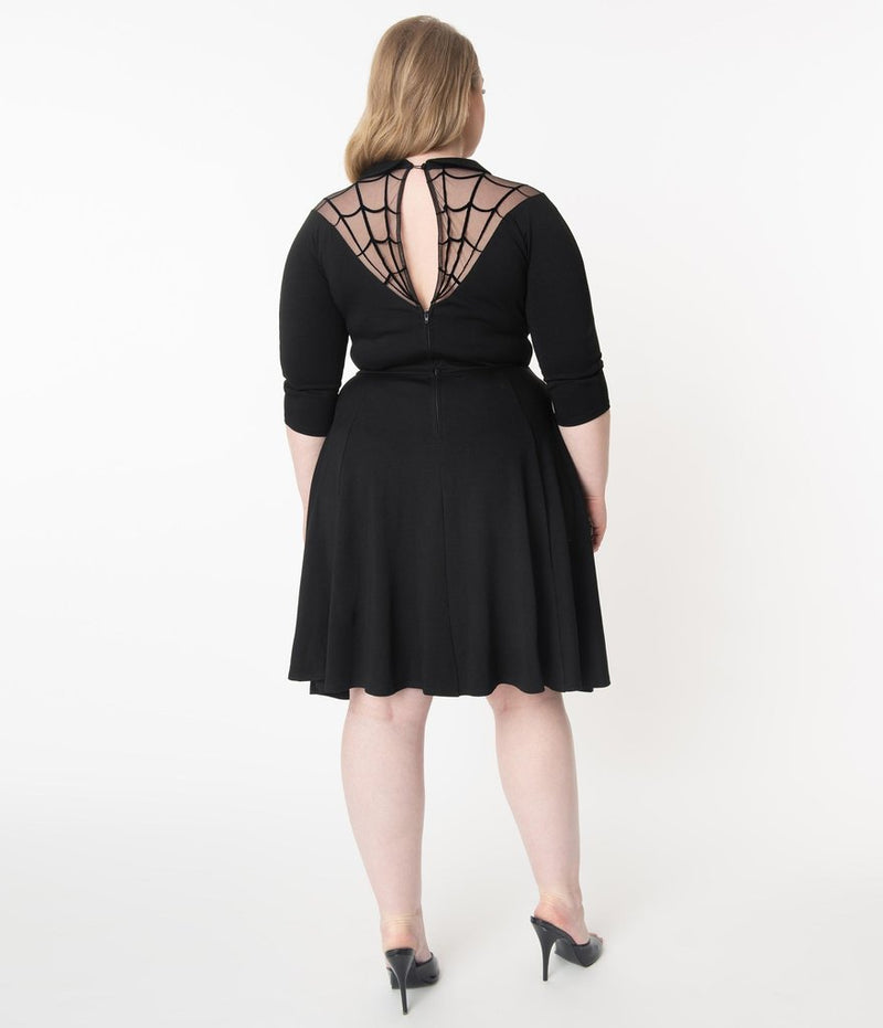 This is a black Unique Vintage flare dress that has a spiderweb neck, Peter Pan collar, 3/4 sleeves and the plus model is wearing black shoes and her hair to the side.
