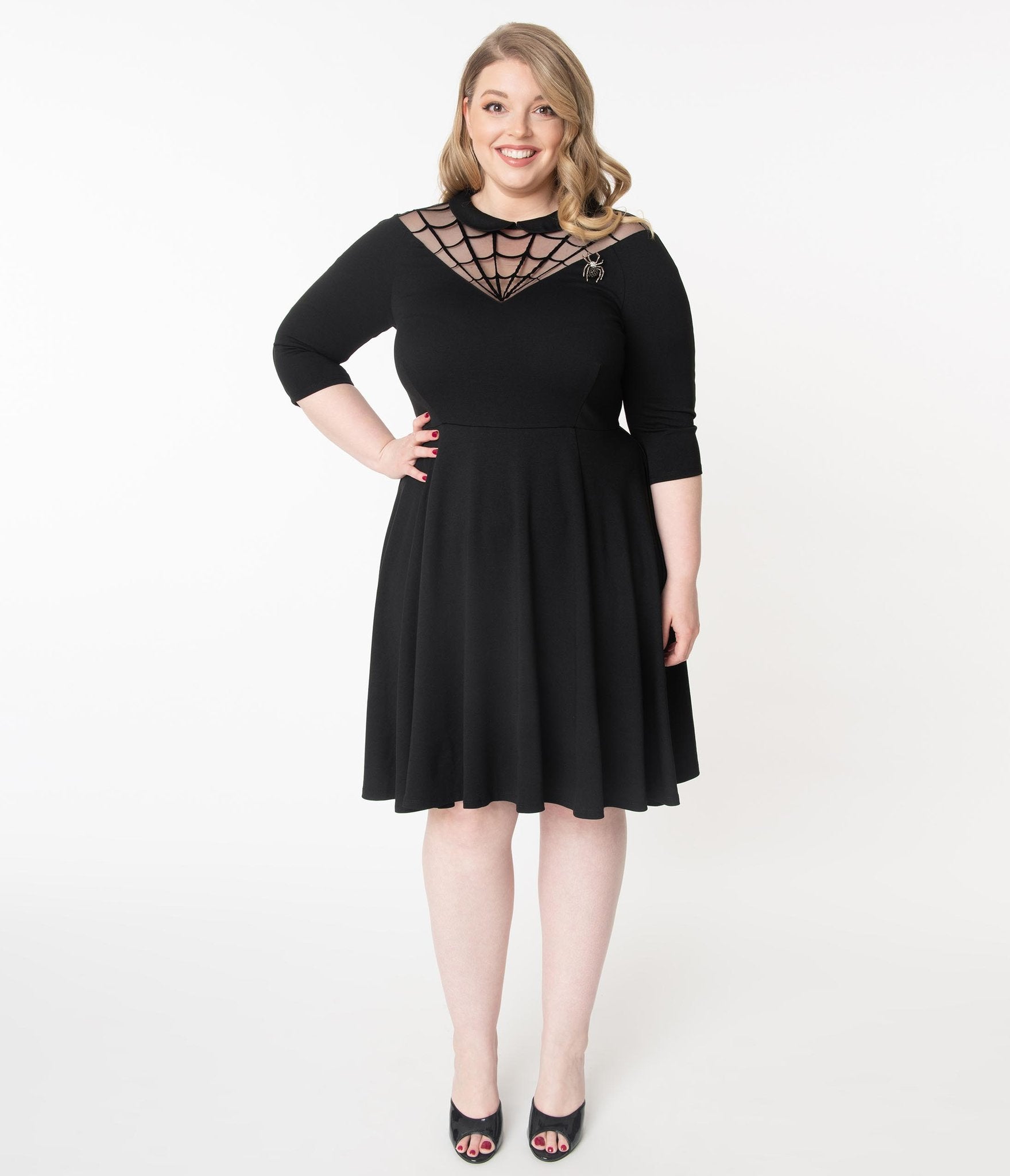 This is a black Unique Vintage flare dress that has a spiderweb neck, Peter Pan collar, 3/4 sleeves and the plus model is wearing black shoes.