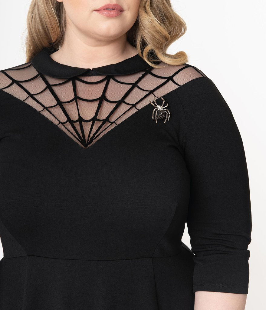 This is a black Unique Vintage flare dress that has a spiderweb neck, Peter Pan collar, 3/4 sleeves and the plus model is smiling and has a jewel spider brooch. 