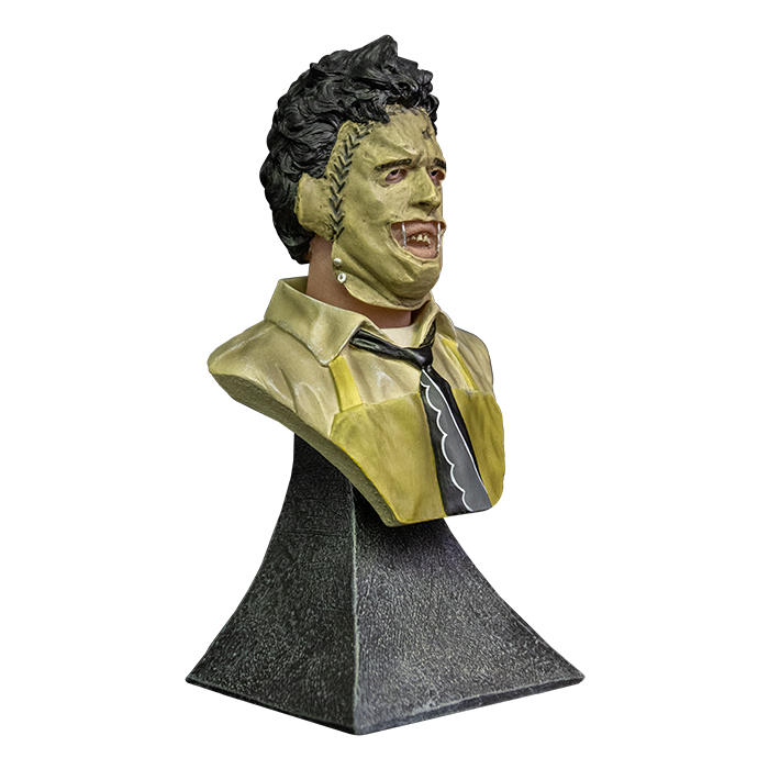 This is a Texas Chainsaw Massacre Leatherface mini bust and  he has brown hair, mask with stitches, yellow apron, tie and is on a grey stand.