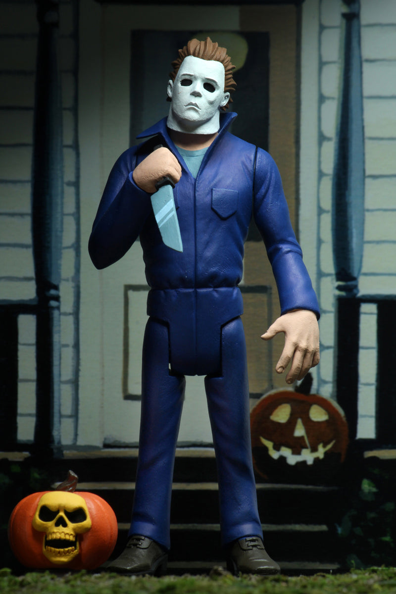 Michael Myers is standing in blue coveralls on a front porch of a house in Haddonfield, holding a knife, with a pumpkin at his feet.
