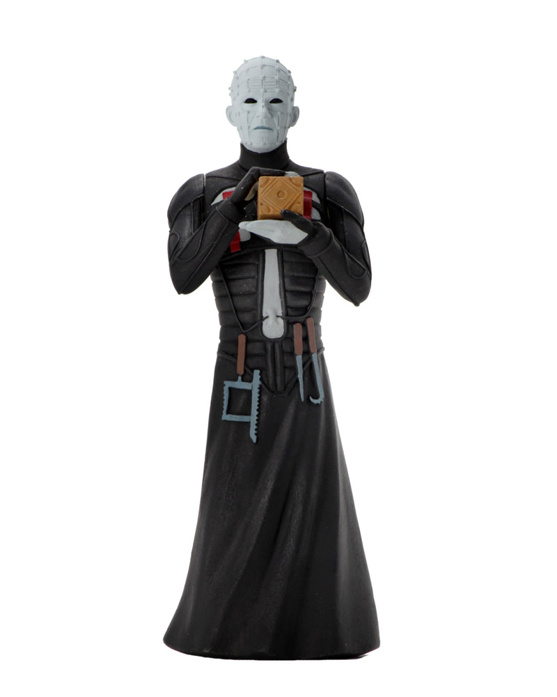 Pinhead NECA action figure is standing in a black dress outfit with tools hanging from it, holding a brown box, with white lighting.