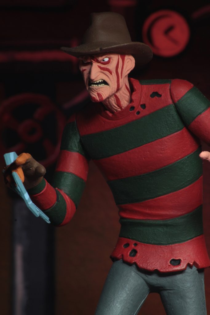 This is a A Nightmare On Elm Street Freddy Krueger posable NECA 6" action figure, who has a glove with knives and is wearing a red and green striped sweater, brown hat and grey pants.