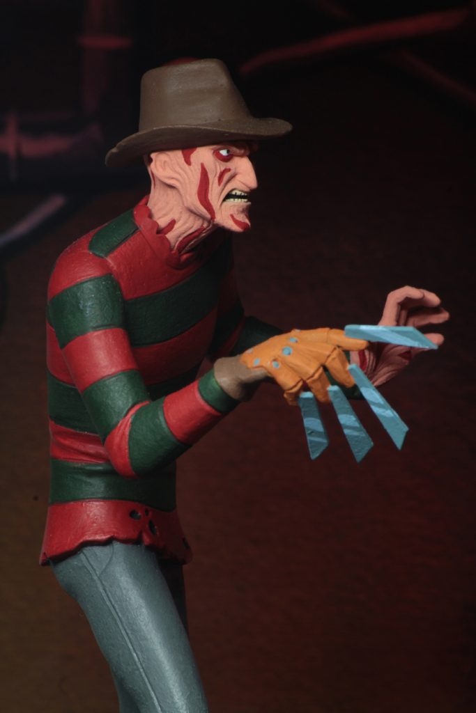 This is a A Nightmare On Elm Street Freddy Krueger posable NECA 6" action figure with blood on his face, who has a glove with blades and is wearing a red and green striped sweater, brown hat and grey pants.