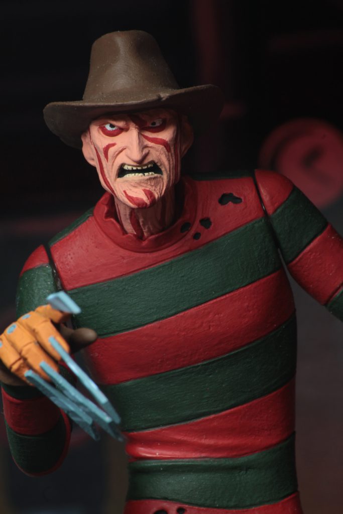 This is a NECA Toony Terror action figure of Nightmare On Elm Street Freddy Krueger, who is wearing a brown hat, red and green sweater and grey pants and who has blood on his face.