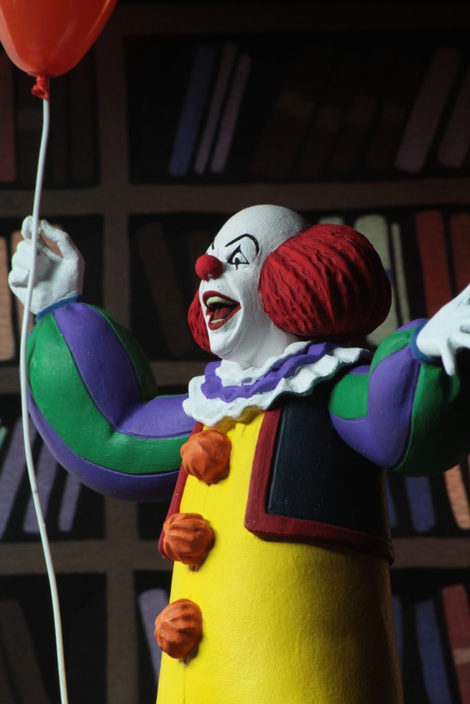 This is a NECA Toony Terrors action figure of 1990 It Movie of Pennywise, who is wearing a yellow clown suit with red balls, who has a white face and red hair and red nose, while holding a red balloon. 