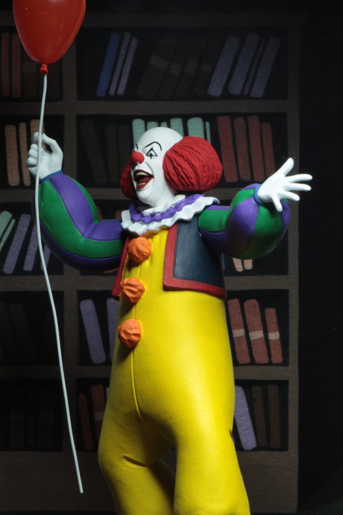 This is a NECA Toony Terrors action figure of 1990 It Movie of Pennywise, who is wearing a yellow clown suit with red balls and white gloves, who has a white face and red hair and red nose, while holding a red balloon. 