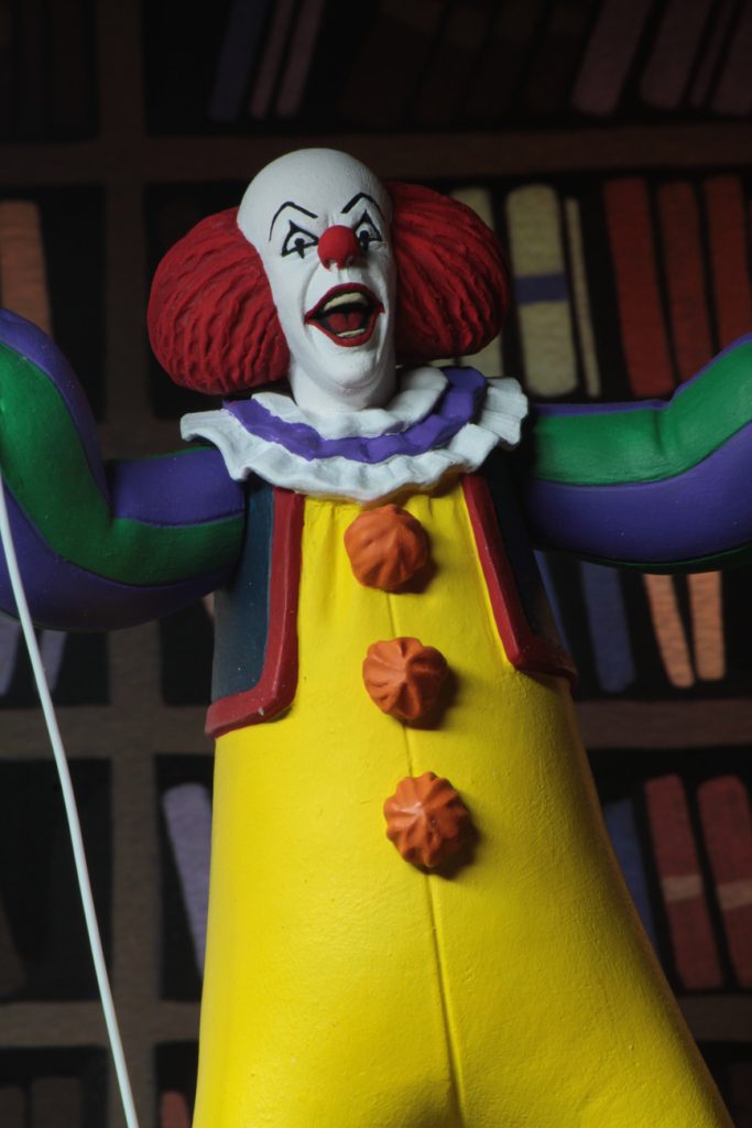 This is a NECA Toony Terrors action figure of 1990 It Movie of Pennywise, who is wearing a yellow clown suit with red balls and green sleeves, who has a white face and red hair, while holding a red balloon. 
