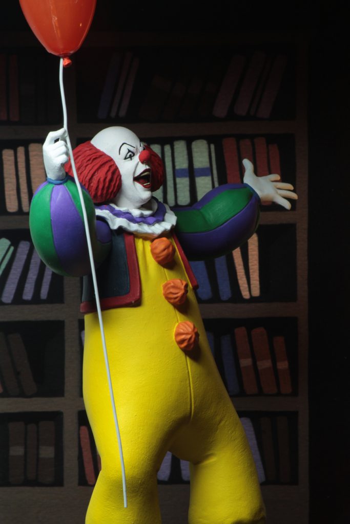 This is a NECA Toony Terrors action figure of 1990 It Movie of Pennywise, who is wearing a yellow clown suit with three red balls, who has a white face and red hair, while holding a red balloon. 