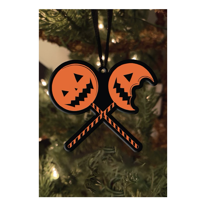 This is a Trick 'R Treat Same bitten lollipop metal ornament that is hanging from a black ribbon and has two orange pumpkins with sticks that are black and orange.