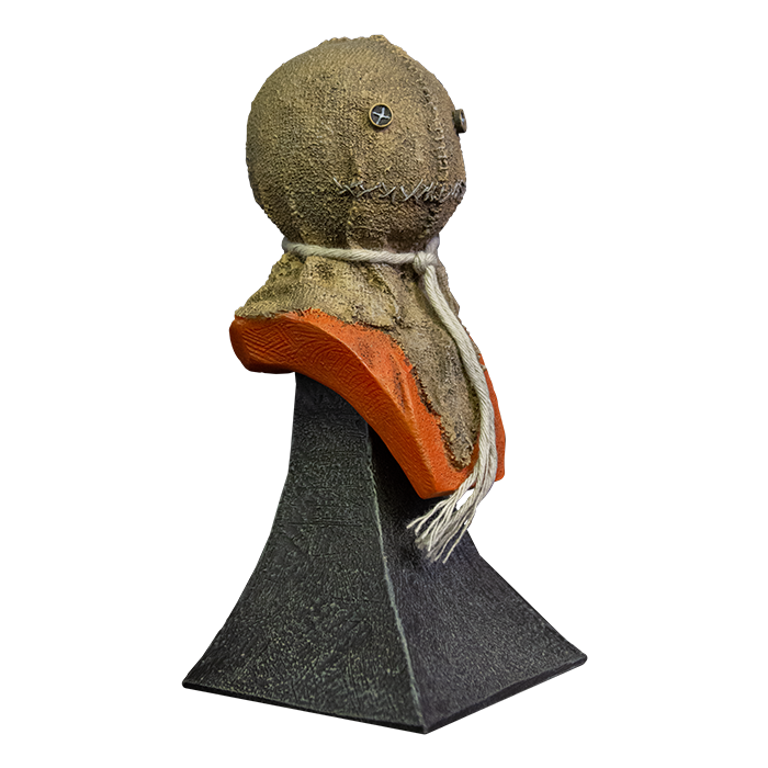 This is a Trick 'r Treat Sam mini bust and he is wearing a burlap mask with button eyes and an orange jumpsuit with a string around his neck and he is on a grey stand.