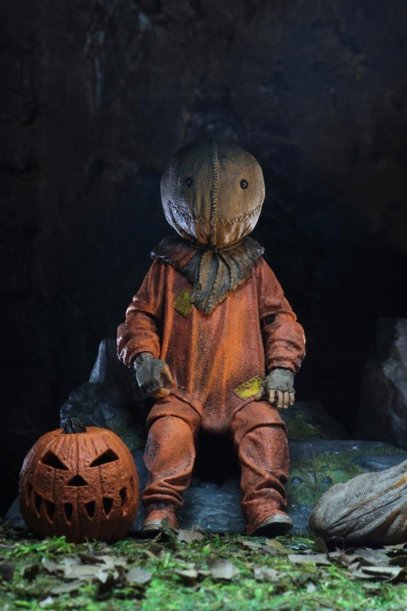 This is a Trick R Treat Sam NECA 7" ultimate action figure and he has a burlap mask, an orange suit, gloves and a pumpkin on the ground.