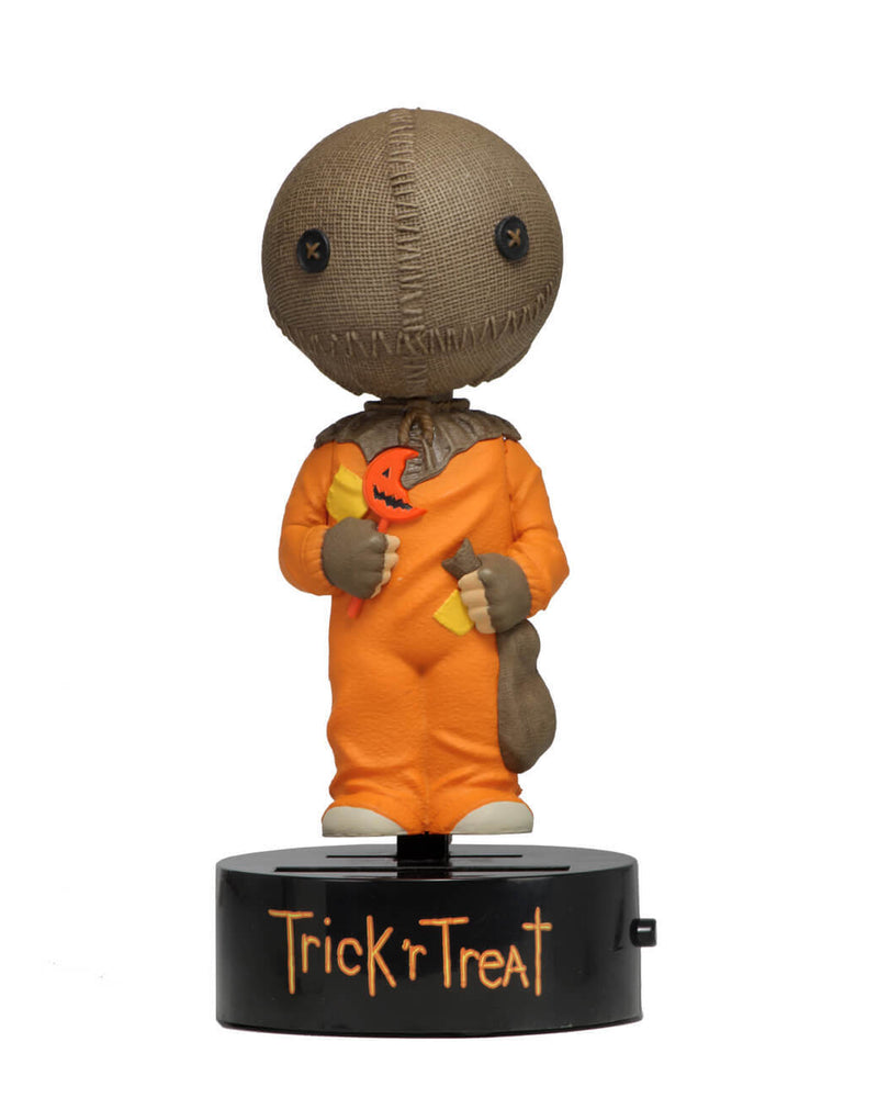 This is a Trick "r Treat Sam NECA Body Knocker and he has a plastic black base, brown burlap head, orange suit and a bitten orange lollipop.
