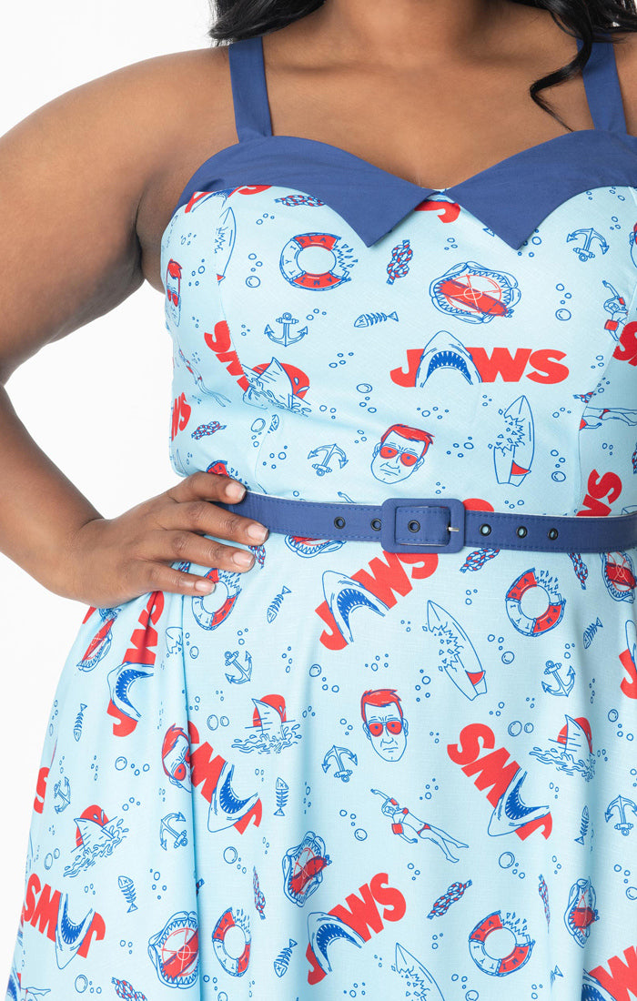 This is a Jaws dress that is light blue and has red text, sharks, lifesavers, Chief Brody and bitten surfboards.