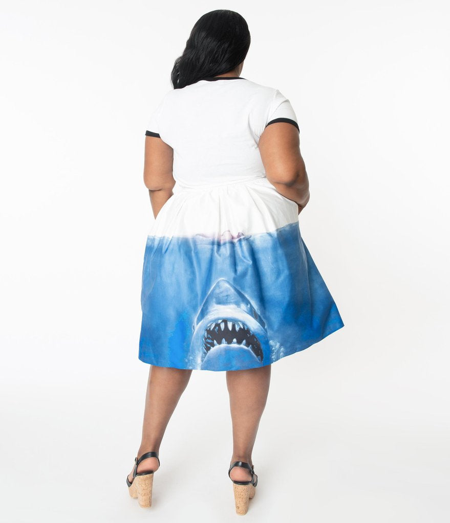 This is a Unique Vintage Jaws movie poster skirt and the model has dark hair, red shoes and the skirt is white at the top, blue water on the bottom and a shark coming up to eat a swimmer, on the back, on a plus size model.