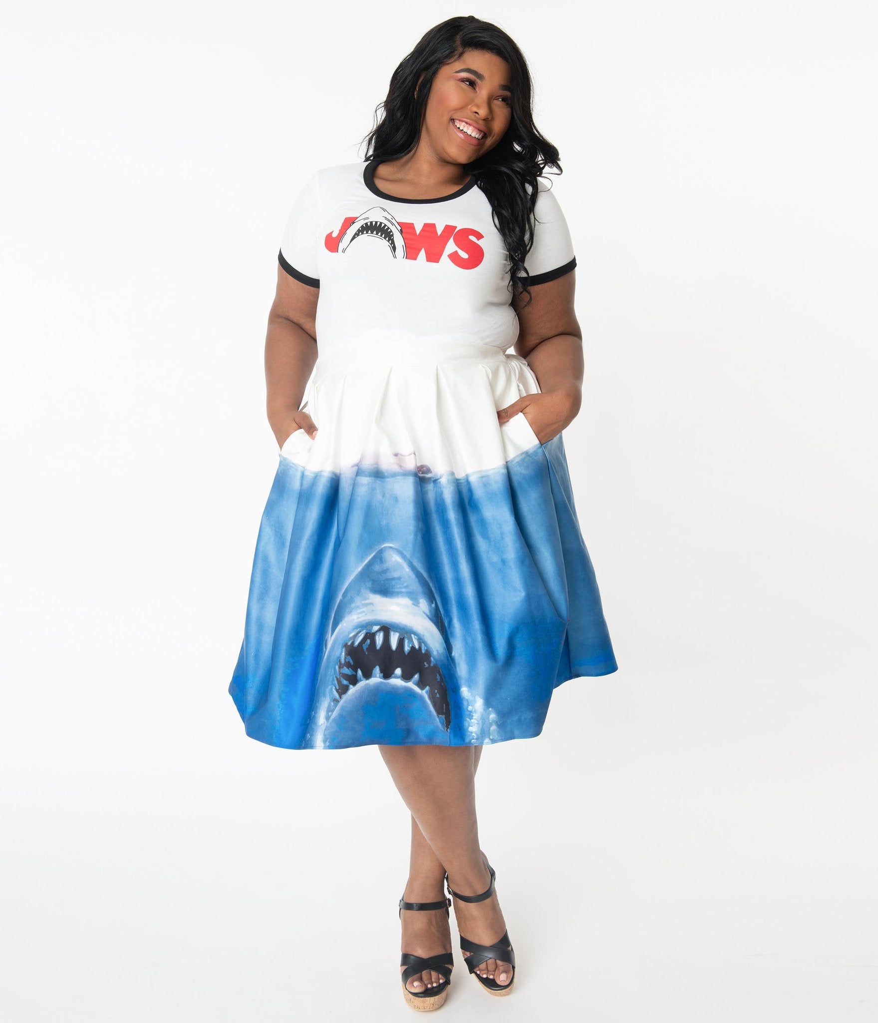 This is a Unique Vintage Jaws movie poster skirt and the model has dark hair, red shoes and the skirt is white at the top, blue water on the bottom and a shark coming up to eat a swimmer, on a plus size model.