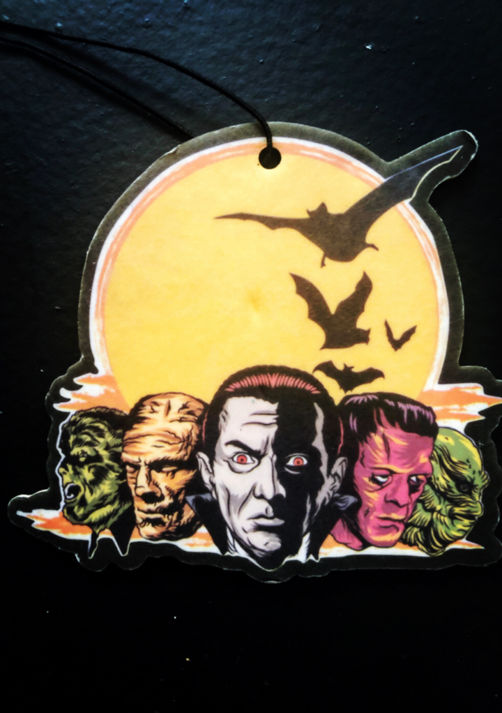 This is a Universal Monsters air freshener that has a green Creature, Frankenstein, Dracula, Mummy and Wolfman, a yellow moon and black bats.