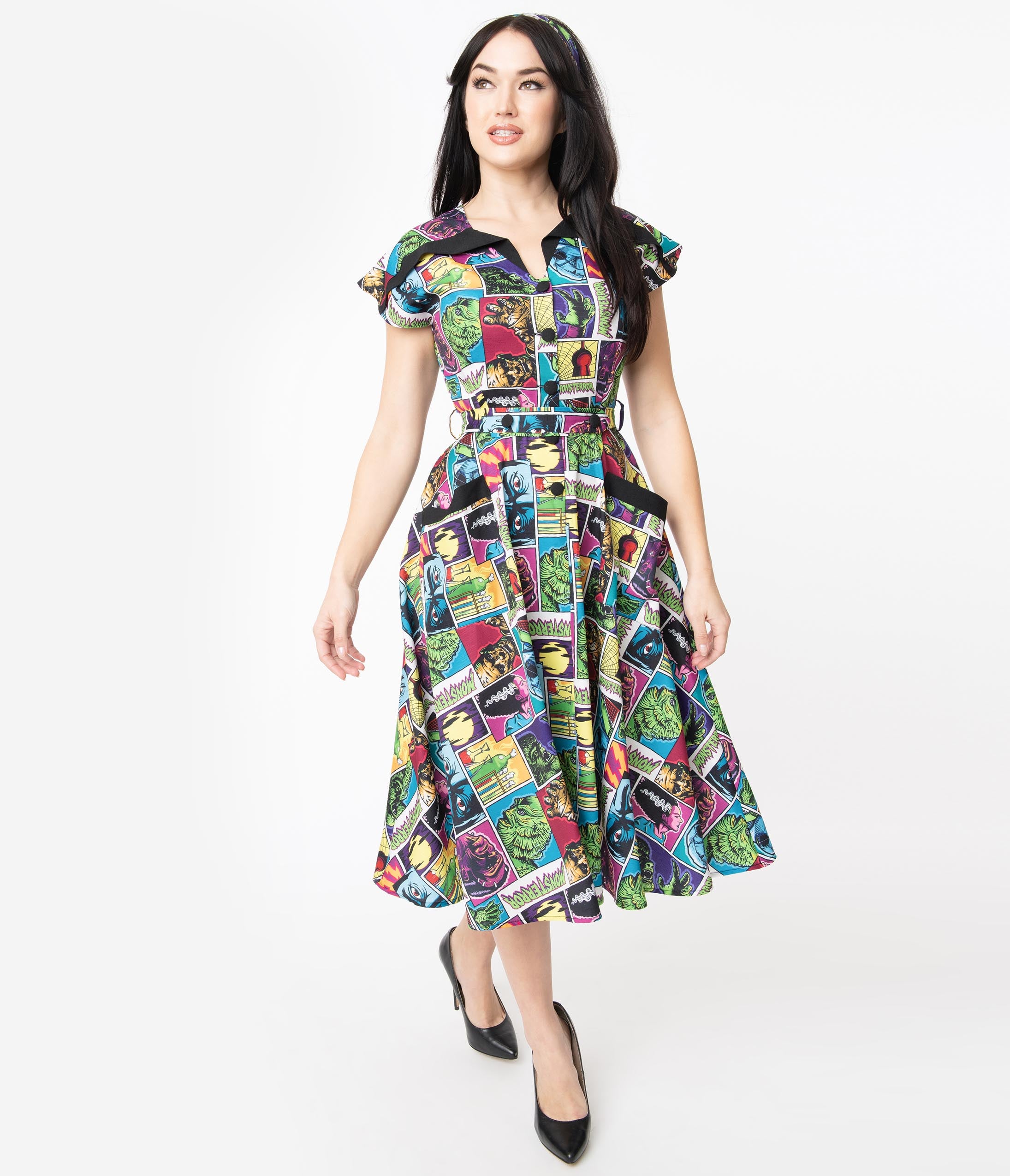 This is a Universal Monsters Hedda dress from Unique Vintage and it has Creature From the Black Lagoon, Frankenstein, Dracula, Mummy, Bride and Wolfman and has a black collar and two pockets and the model is wearing black shoes.