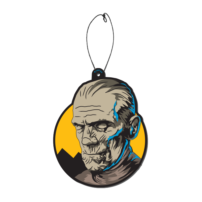 This is a Universal Monsters Mummy air freshener by Trick Or Treat and he has brown weathered skin and ears and is in front of a yellow circle, with a plastic hanger.